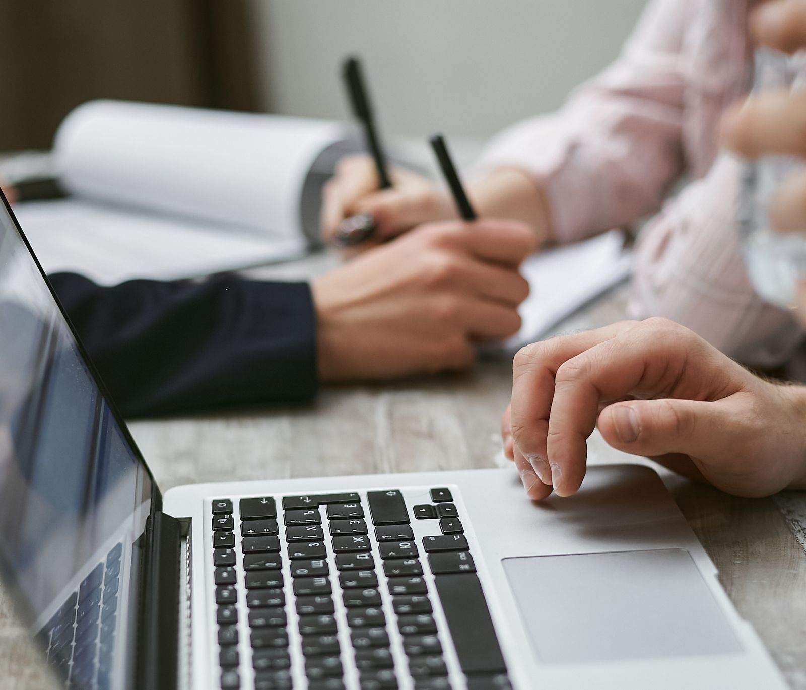 Manos trabajando con un portátil y tomando notas durante una reunión de trabajo