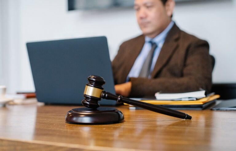 Profesional trabajando en un portátil en un despacho, con documentos y un mazo sobre la mesa